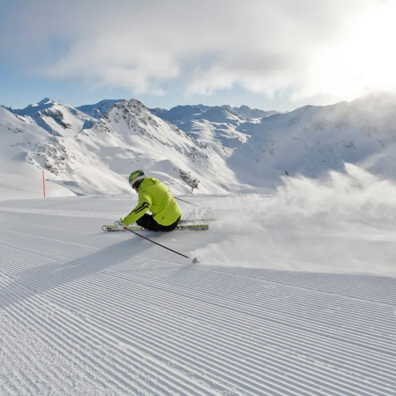 Skier in bright green jacket carving downhill on groomed alpine slope